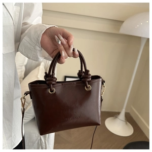 Détail du sac seau en cuir café foncé avec poignée torsadée et anneaux métalliques