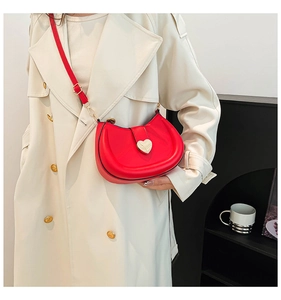 Red candy-colored saddle bag with heart-shaped gold lock worn over a beige trench coat
