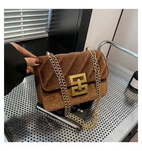 Détail du sac bandoulière en velours marron matelassé avec chaîne dorée sur un livre