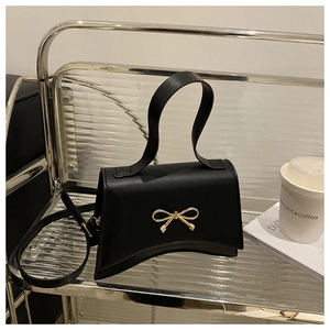 Close-up of black leather hourglass handbag with elegant golden bow buckle and smooth texture
