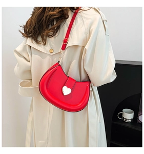 Model wearing a red crescent saddle bag with heart buckle over a stylish beige trench coat