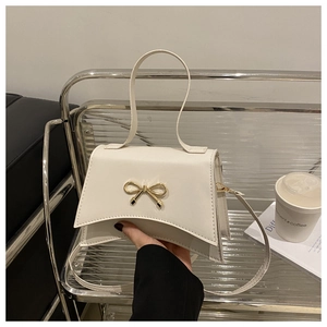Detail of white hourglass handbag featuring golden bow hardware and slim strap