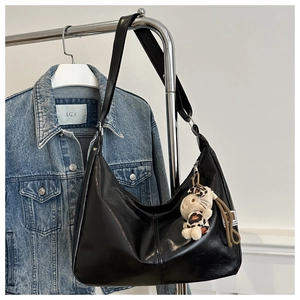 Detail of black leather hobo bag with wide strap and leopard print cat keychain charm