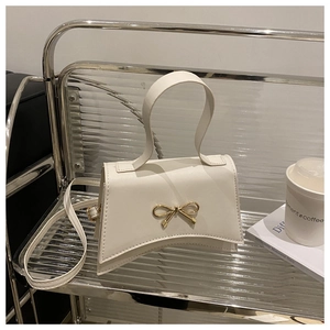 Detailed view of white stylish crossbody bag with gold bow lock and asymmetric base