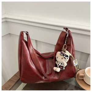 Close-up of vintage red crossbody bag with textured leather and plush kitten pendant