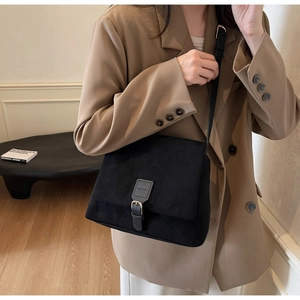 Macro shot of black matte suede leather crossbody bag with vintage buckle on brown blazer