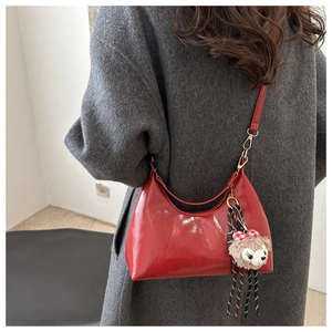 Detail of red glossy patent leather hobo bag with a cute plush bear charm on a grey coat