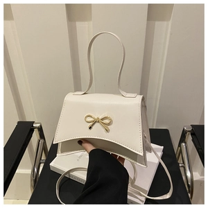 Detail of white leather crossbody bag featuring golden bow ornament and curved base design