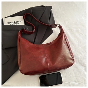 Detail of burgundy hobo bag with adjustable strap and phone for scale on white fabric