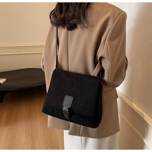 Close-up of a vintage black suede crossbody bag with metal buckle and shoulder strap