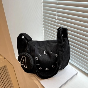 Detail of black corduroy tote bag showing white letter embroidery and round coin purse
