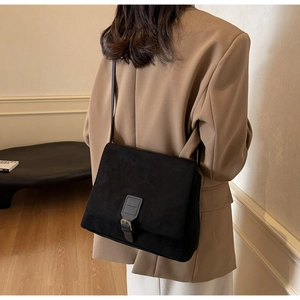 Dettaglio di una borsa a tracolla in pelle scamosciata nera opaca su un blazer color cammello