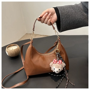Detail of a brown leather crescent shoulder bag with a teddy bear charm attachment