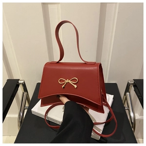 Detail of red trapezoid handbag featuring metal bow accent and smooth matte leather finish