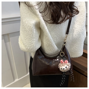 Detail view of dark coffee crescent underarm bag with glossy leather and plush bear charm