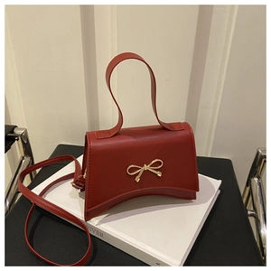 Detail of red bow-knot handbag on white book showing matte PU leather and gold buckle