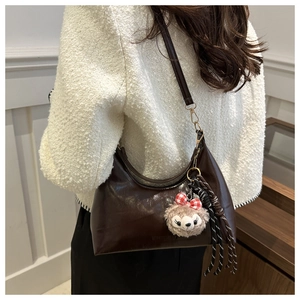Detail of dark brown crescent hobo bag with plush charm on a model in tweed outfit