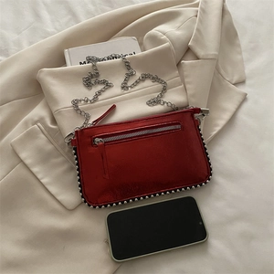 Red metallic chain bag with silver rivets, styled with a beige blazer and smartphone