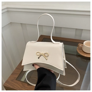 Close-up of white leather crossbody bag featuring an elegant gold bow metal clasp