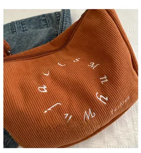 Close-up of brown corduroy tote bag featuring white embroidered letters on denim background