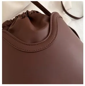 Close-up of matte brown leather bucket bag showing fine double stitching and drawstring