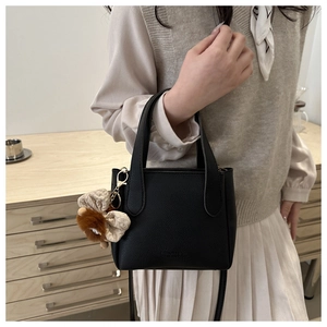 Detail of black leather bucket bag with top handles and a brown plush animal charm