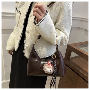 Detail of a brown glossy crescent shoulder bag with a plush bear charm on white tweed coat