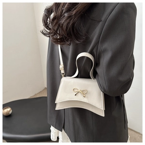 Detail of cream crossbody bag with golden bow hardware shown on a model