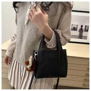 Detail of black lychee grain leather bucket bag with plush charm and bow accessory
