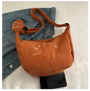 Detail view of orange corduroy crossbody bag with coin purse and size comparison to phone