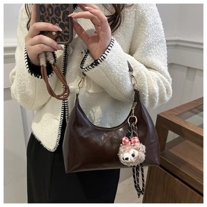 Detail view of dark coffee semi-moon underarm bag with glossy finish and plush charm