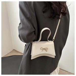 Detail of cream white leather handbag with golden bow buckle on grey blazer