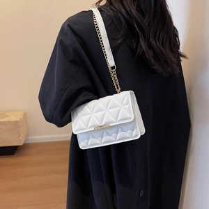 White quilted crossbody bag with gold chain strap shown on model in a minimalist setting