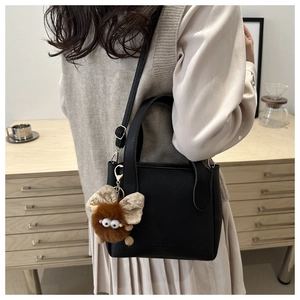 Close-up of black lychee grain leather handbag with brown plush monster bag charm