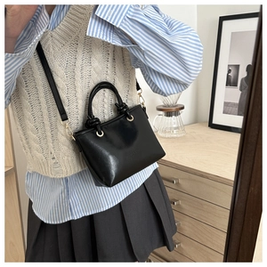 Detail of minimalist black leather handbag with circular ring handle and gold hardware