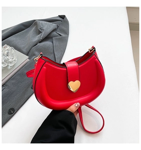 Close-up of a red leather saddle bag with a large gold heart buckle and thin shoulder strap