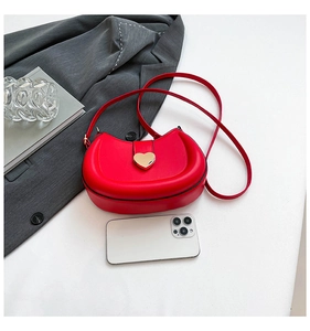 Mini red saddle bag with gold heart clasp shown beside smartphone for size comparison