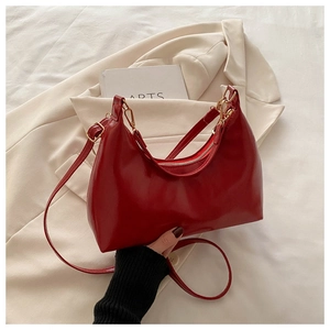 Close-up of red glossy underarm bag with gold metal zipper and adjustable strap