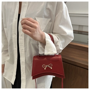 Detail of red leather mini handbag with gold bow clasp and unique curved bottom silhouette
