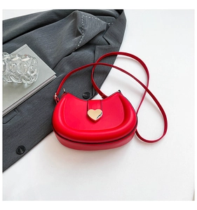 Detail of red leather saddle bag with a golden heart-shaped clasp on white surface