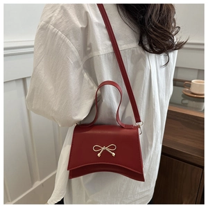 Red crossbody bag with gold bow detail shown on a model against a cream wall