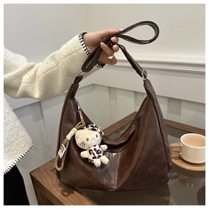 Detail of dark brown glossy PU leather hobo bag with a plush leopard charm and wide strap