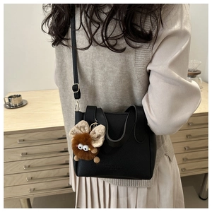 Détail du sac seau noir en cuir grainé avec un pendentif monstre en peluche marron doux