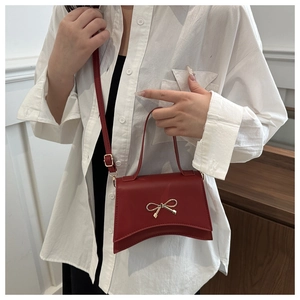Detail view of a red leather crossbody bag featuring a golden bow buckle on the flap