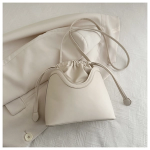 Detail of a minimalist beige drawstring bucket bag resting on a matching blazer fabric