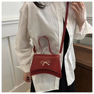 Détail du sac à bandoulière rouge avec nœud en métal et finition en similicuir lisse