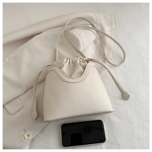 Detailed comparison of the cream bucket bag size next to a smartphone for scale