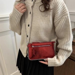 Glossy red crossbody bag with silver rivets and metal chain strap on model
