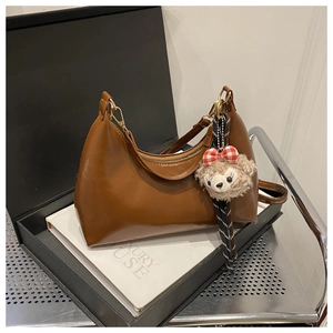 Detail of caramel brown underarm bag with cute plush bear charm in a black gift box