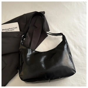 Flat lay of a black glossy leather hobo bag with adjustable strap on business attire